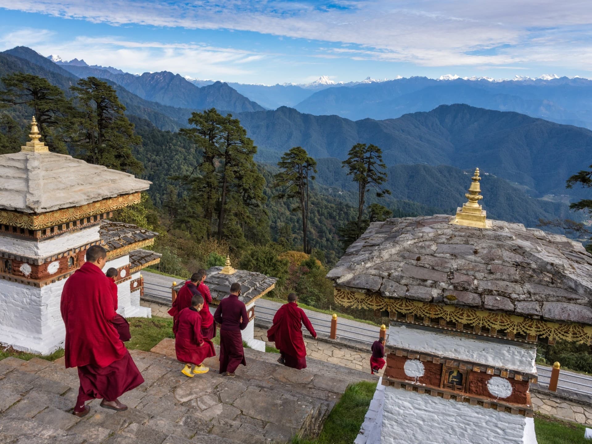 Young monks in crimson robes descending the chortens at Dochula Pass with the eastern Himalayas beyond