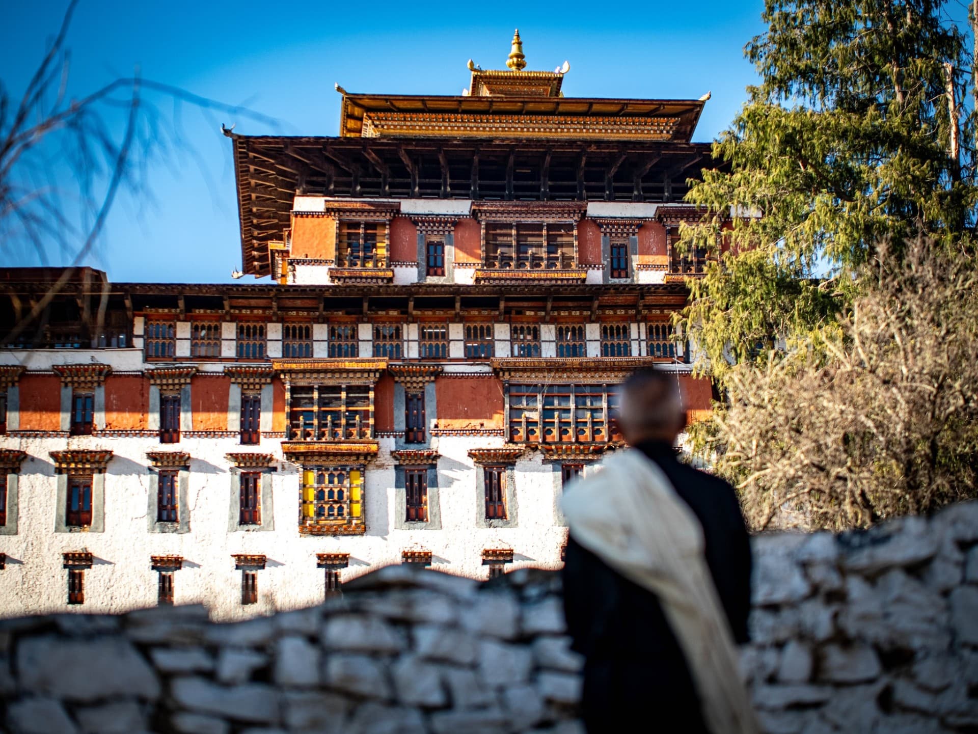 A monk in white kabney before a Bhutanese dzong at golden hour