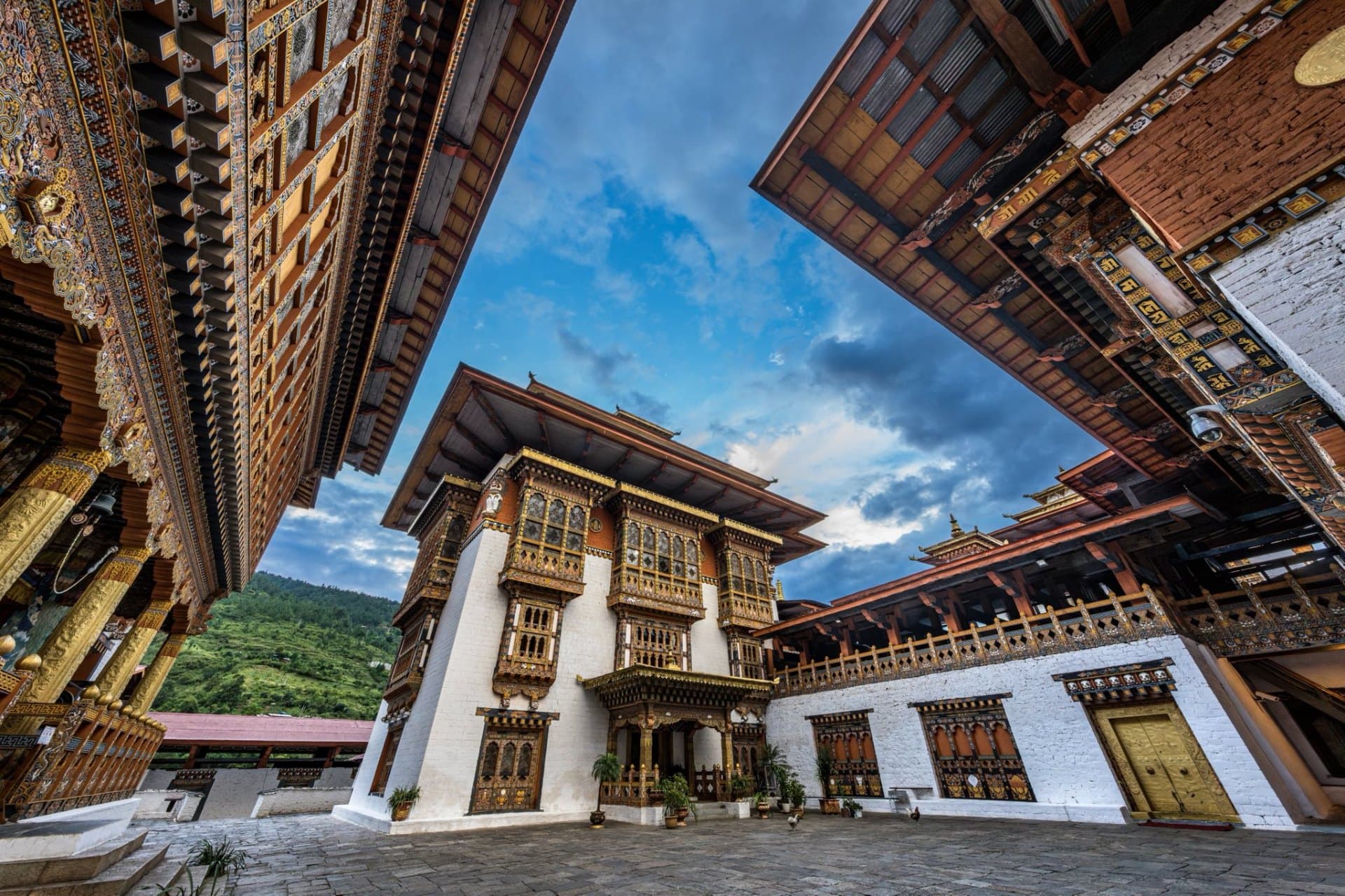 The painted courtyard of a Bhutanese dzong rising into a clouded blue sky