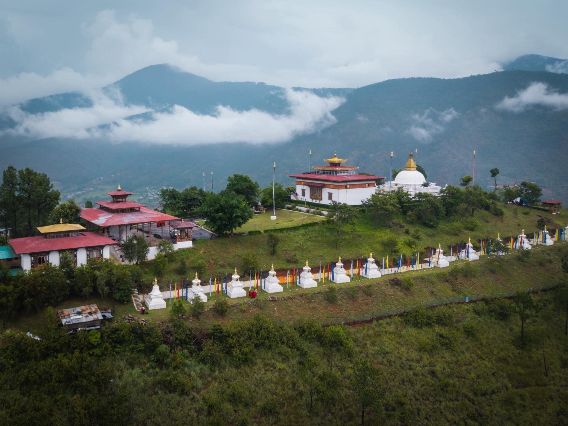 A monastery and stupas perched above a misted Bhutanese valley