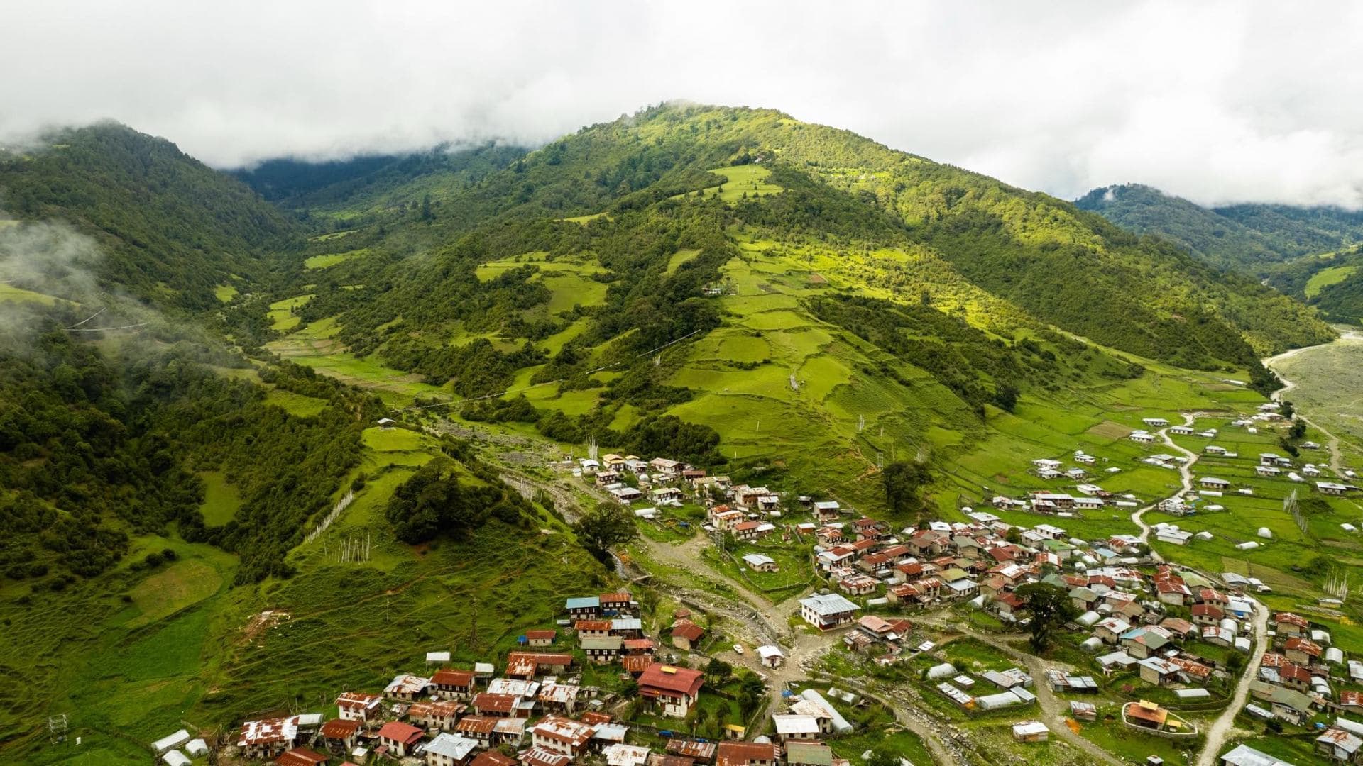 Aerial view of a remote Bhutanese village nestled in mist-veiled green Himalayan slopes