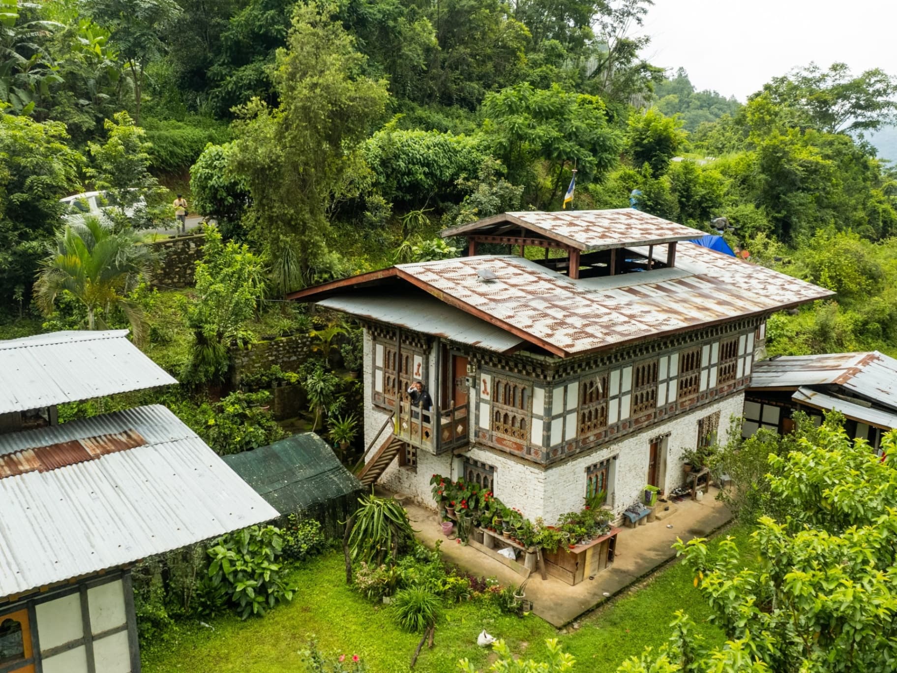 A traditional Bhutanese farmhouse with painted timber facade and patterned tin roof, set among dense jungle hillsides